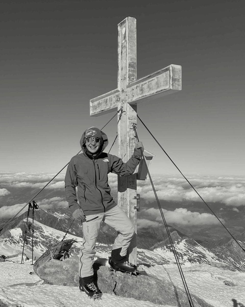 Felix Schenet am Gipfelkreuz des Kitzsteinhorns, dahinter ein Meer aus Wolken